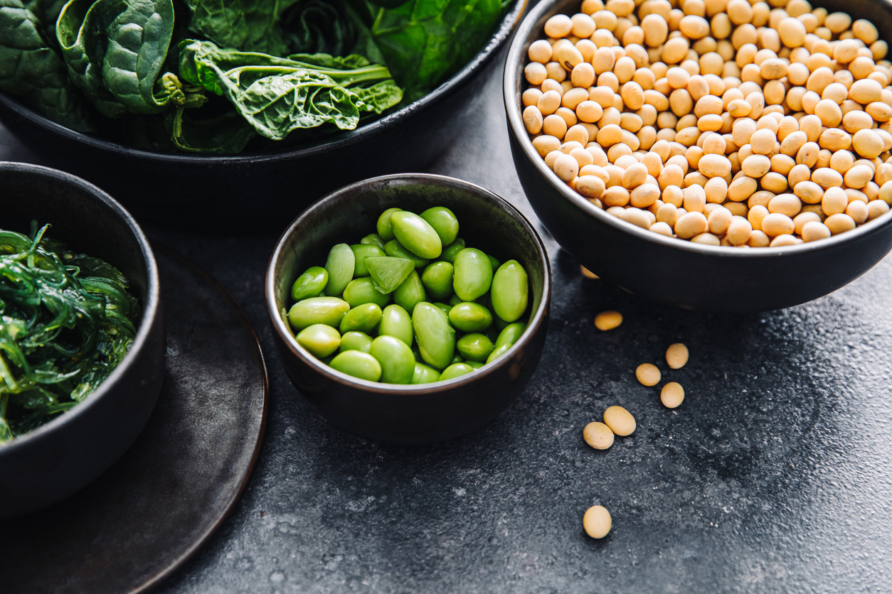 Close-up of raw vitamin E rich food in bowls on black table. Fresh green spinach, edamame, wakame and lentil seeds in bowls on a table.
