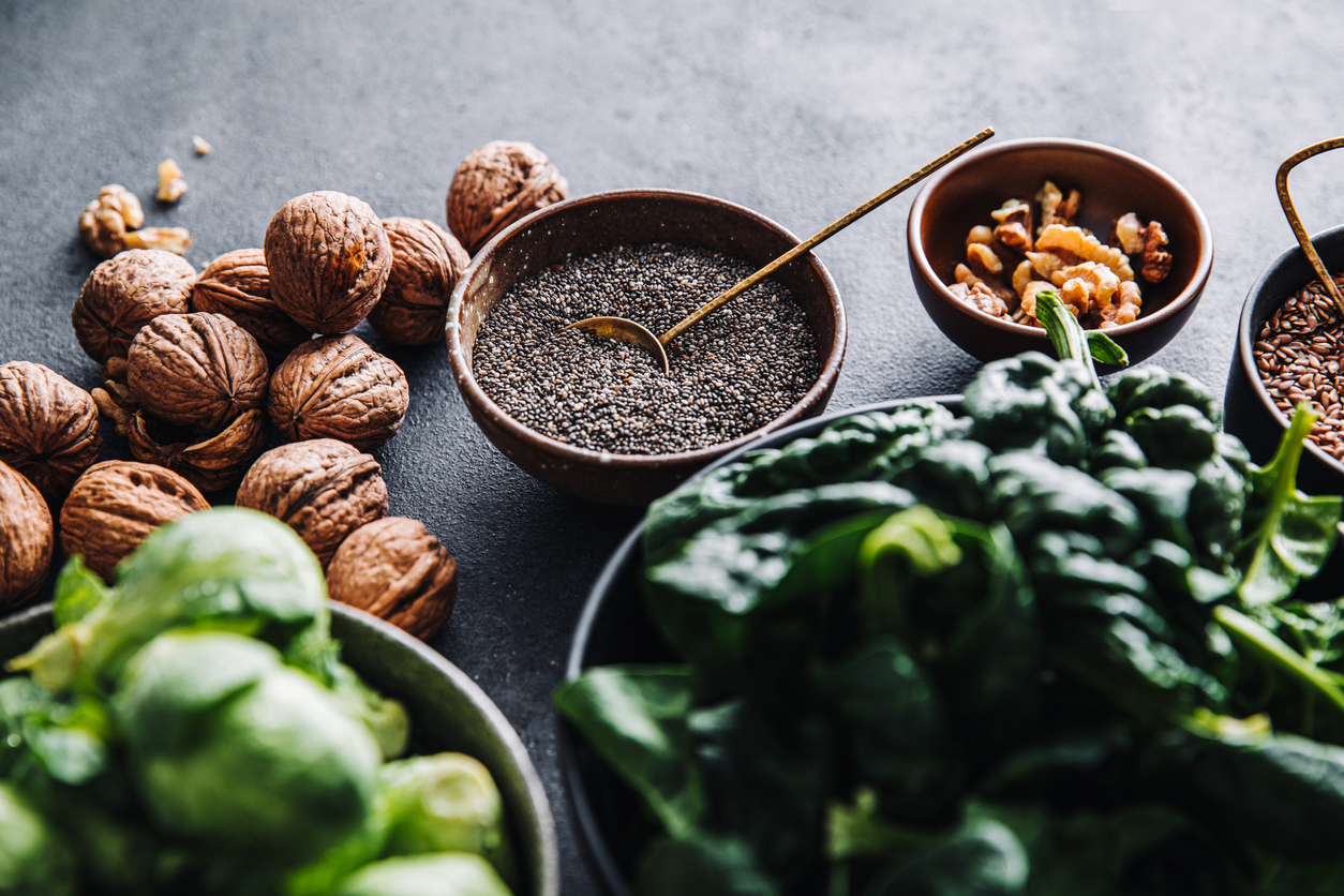 Close-up of omega 3 vegan food in bowls on black table. Fresh green spinach, flax seeds, walnuts, and brussel sprouts in bowls on a table.