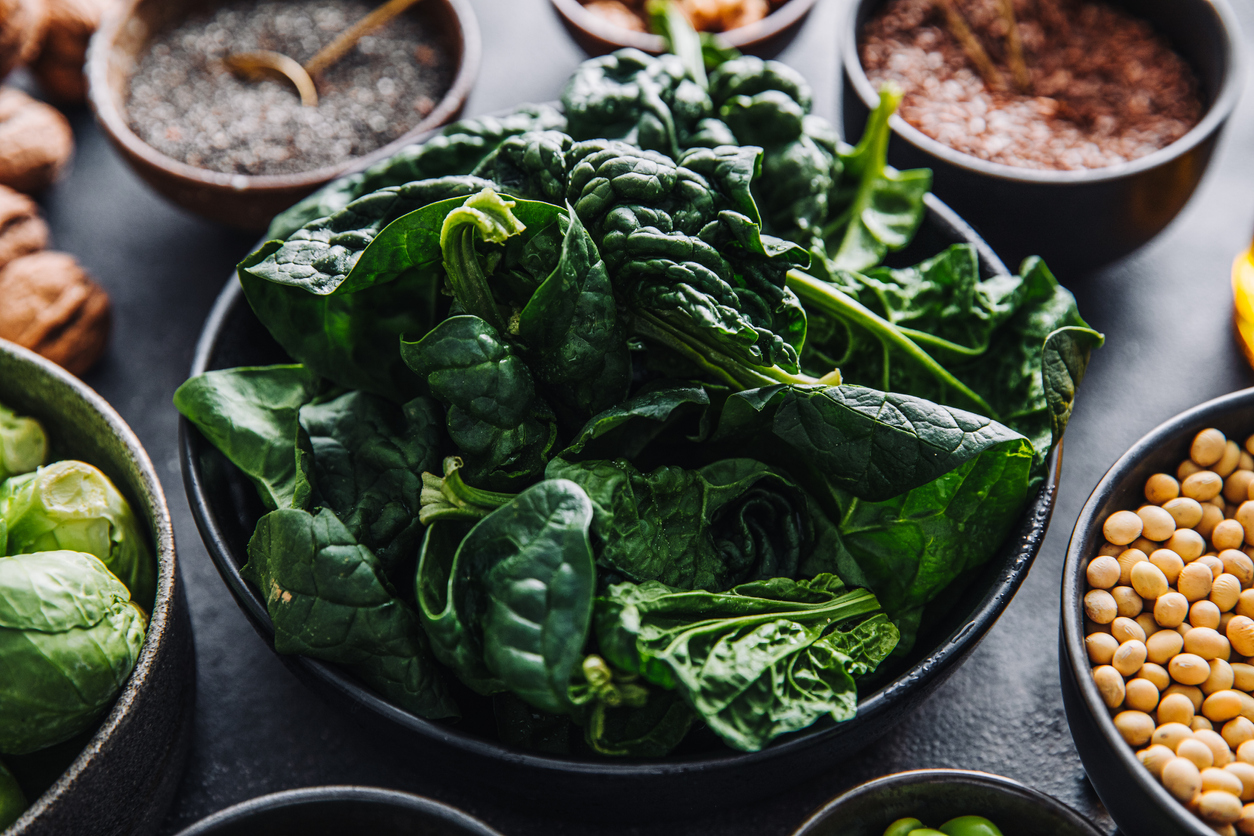 Close-up of omega 3 vegan food ingredients on the table. Fresh green spinach in a bowl with flax seeds, walnuts, brussel sprouts, and lentil seeds in bowls.