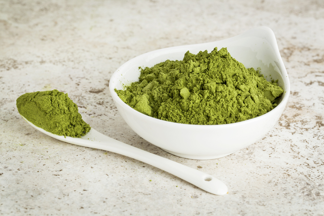 moringa leaf powder in a small bowl with a spoon against a ceramic tile background